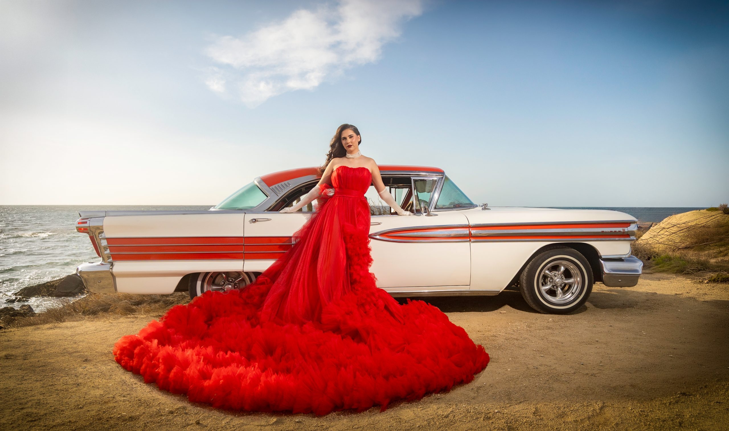 Vintage convertible and model in a red gown by the sea